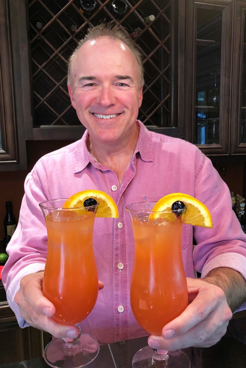 man in a pink shirt holding two hurricane cocktails
